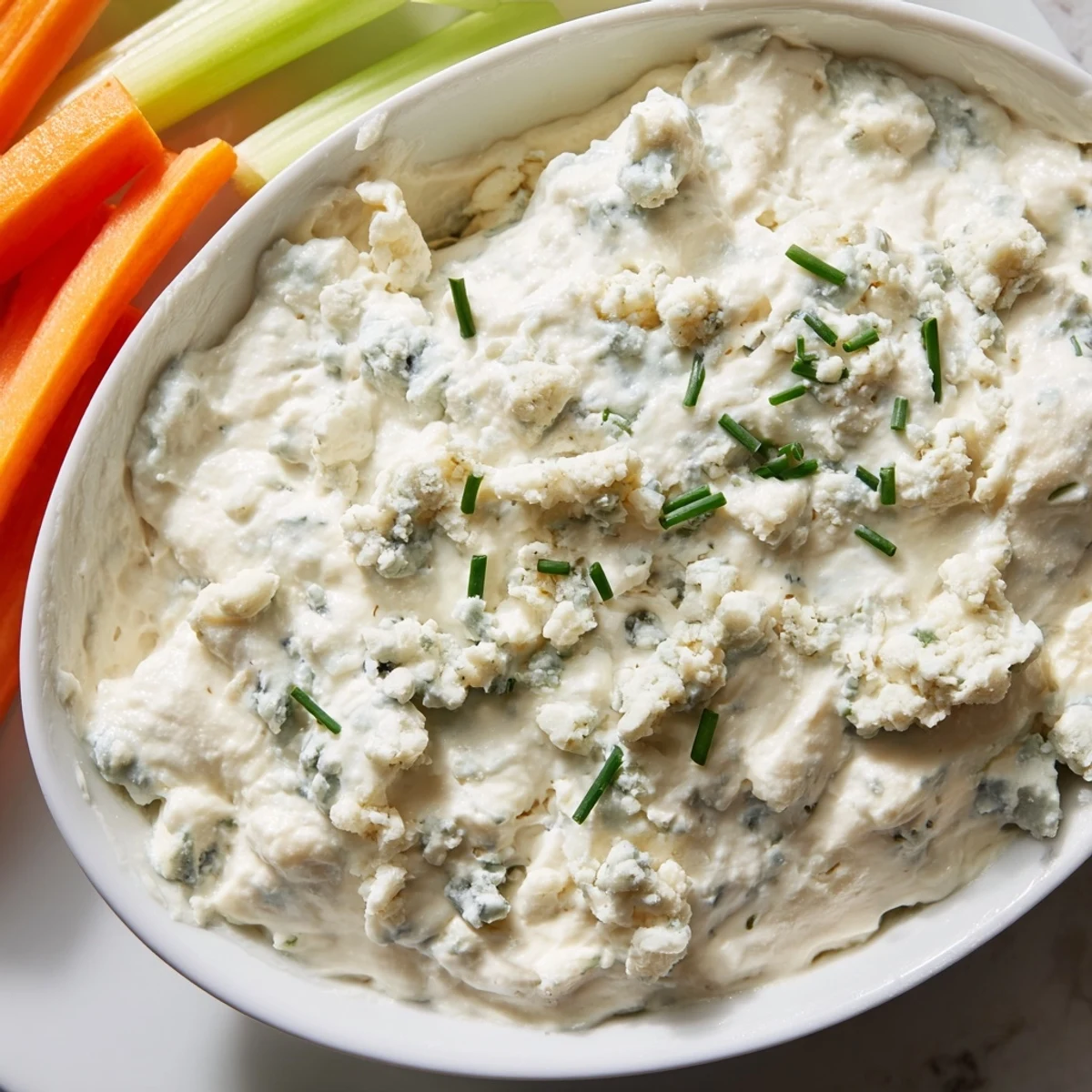 Creamy blue cheese dip served in a bowl with fresh celery sticks and carrot sticks nearby.