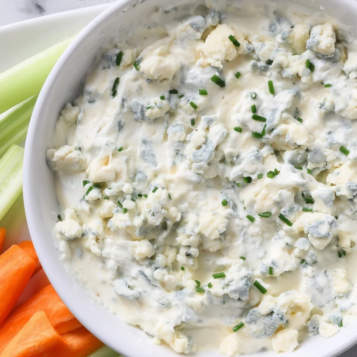 Thick blue cheese dip topped with crumbled cheese and chopped chives in a rustic bowl.