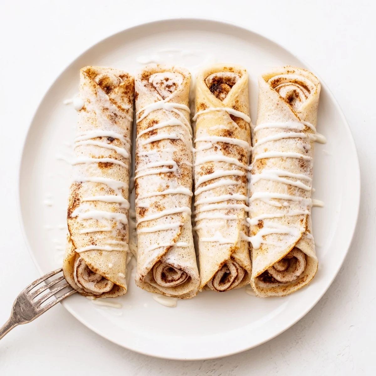 Golden cinnamon roll protein crepes drizzled with sweet vanilla glaze on a warm plate