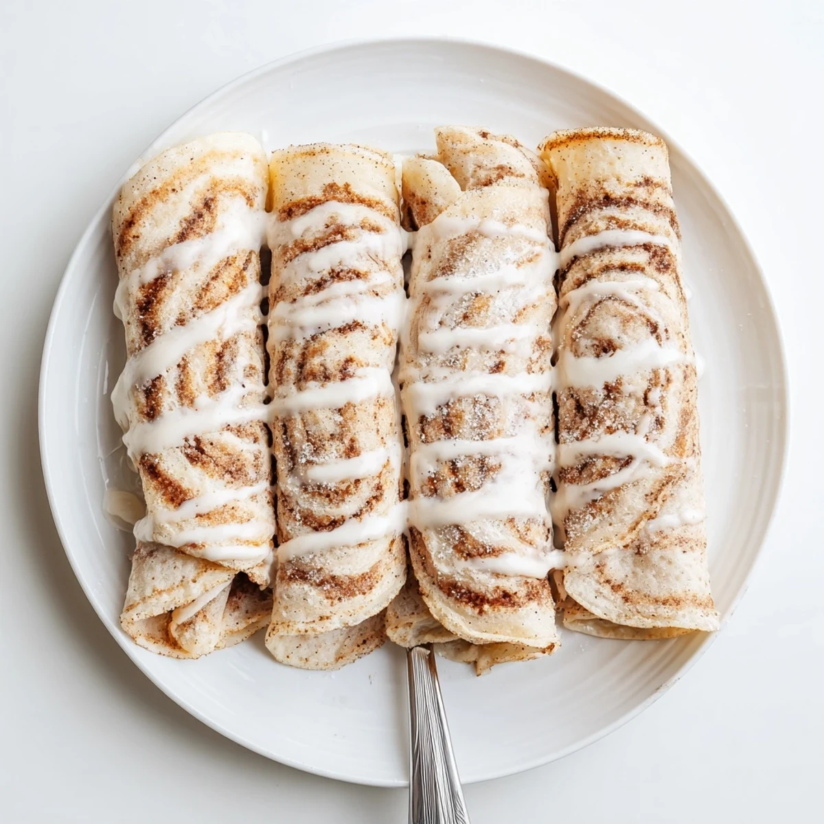 Rolled cinnamon protein crepes oozing with creamy cinnamon swirl filling and powdered sugar glaze
