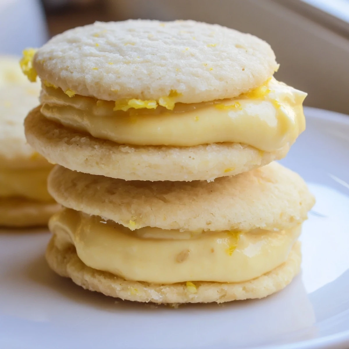 Soft vegan lemon sandwich cookies dusted with powdered sugar beside a teacup