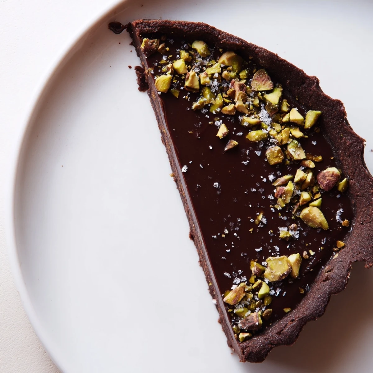 Silky dark chocolate pistachio tart in a cocoa crust topped with vibrant green pistachios