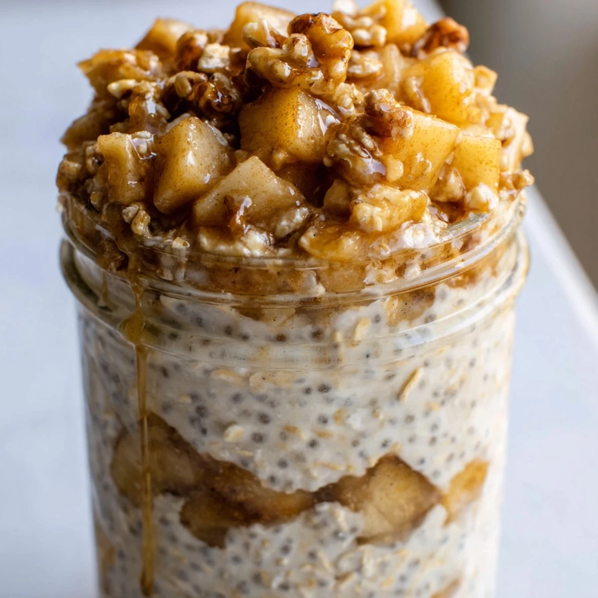 Creamy apple crumble overnight oats layered in a mason jar with cinnamon apple chunks and crunchy walnut topping