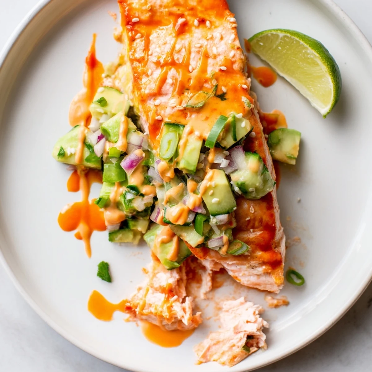 Golden Bang Bang Salmon fillet resting on a bed of fresh avocado cucumber salsa with sesame garnish
