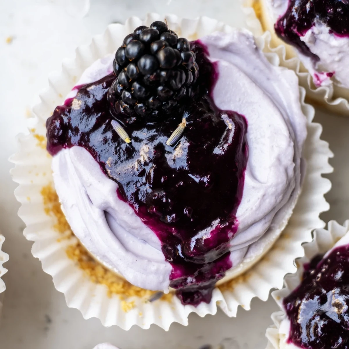 Creamy Mini Blackberry Lavender Cheesecakes in paper liners with fresh berries and sprigs of lavender
