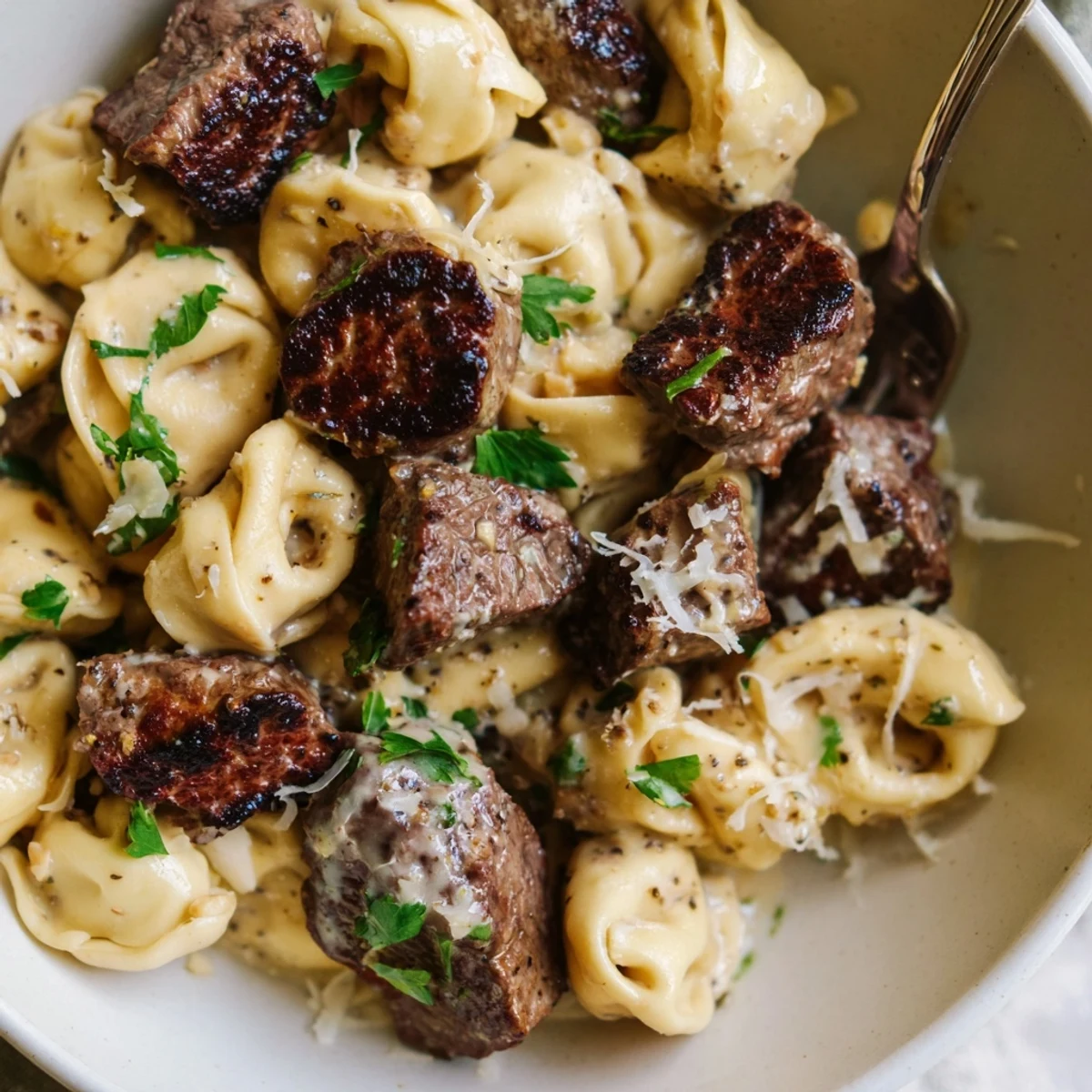 Golden seared steak bites served over cheese tortellini in garlic cream sauce