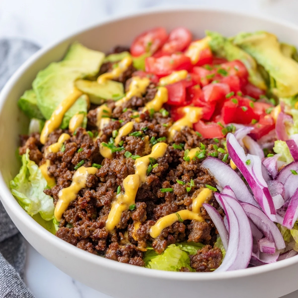 Juicy ground beef burger bowls topped with avocado, pickles, and tangy sauce