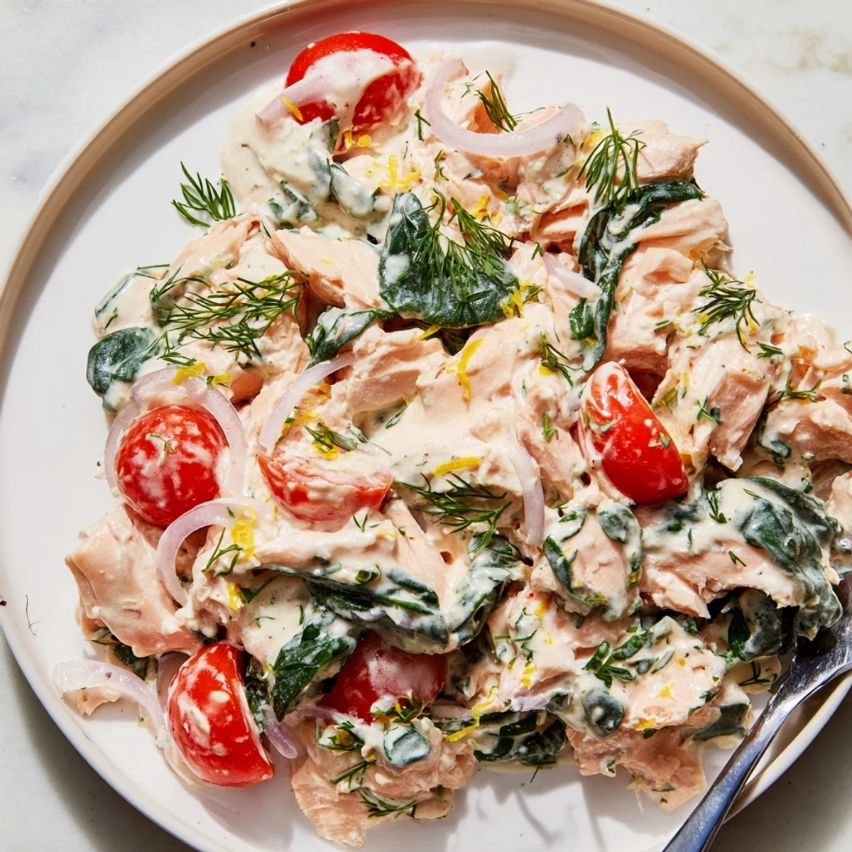 Creamy leftover salmon recipe served in a skillet with wilted spinach and cherry tomatoes