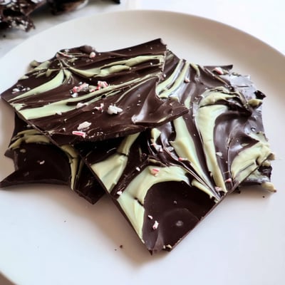 Mint chocolate bark with white chocolate swirls on a dark slate backdrop, ready to serve after chilling with a hot cup of coffee.  