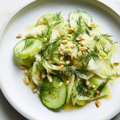 Vibrant bowl of crisp fennel cucumber salad topped with lemon zest and pine nuts  